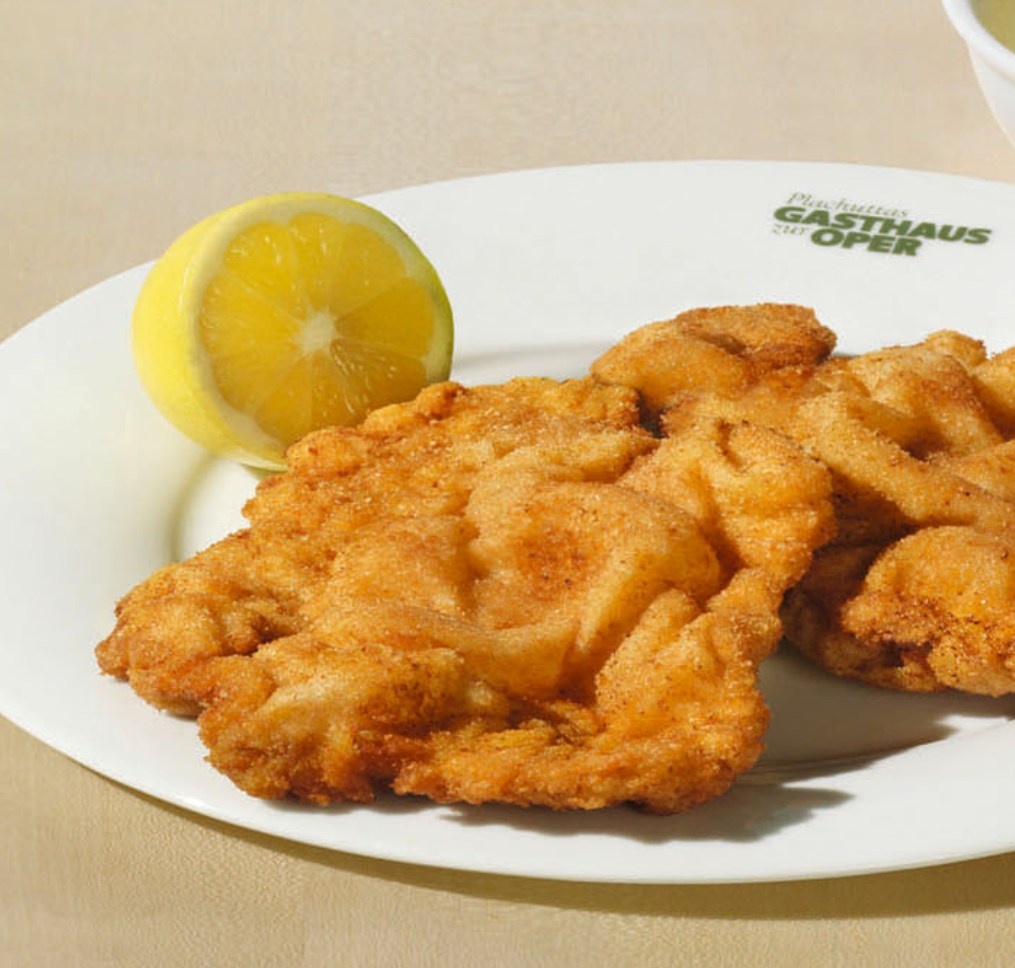 Zwei panierte und gebratene Schnitzel auf einem weißen Teller mit einer Zitronenspalte.