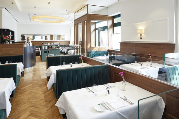 Helles, modernes Restaurant mit grünen Ständen, weißen Tischtüchern und einer Hostess am Eingang.