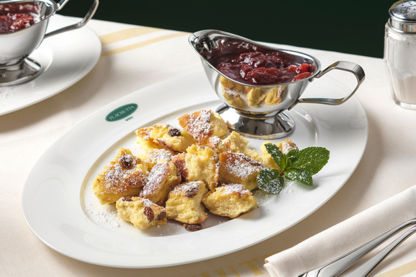 Reihen von Weinstöcken in einem sonnigen Weinberg mit einer Stadt und Hügeln in der Ferne unter einem teilweise bewölkten Himmel.