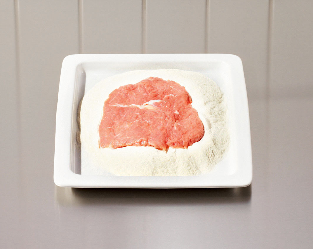 Rohes Fleisch auf einem Mehlhaufen auf einem weißen, quadratischen Teller auf einer grauen Arbeitsplatte.