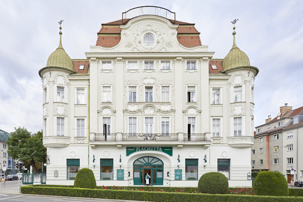 Elegant white historic building with ornate details, green doors and round towers on each side.