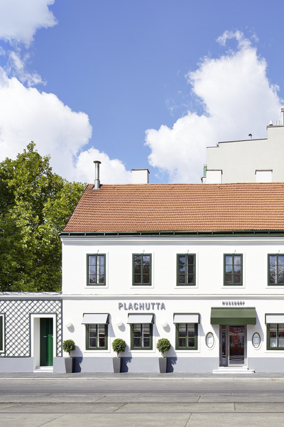 Moderne Holzpergola mit Sitzgelegenheiten auf einer Rasenfläche, durch das Lamellendach fällt das Sonnenlicht.
