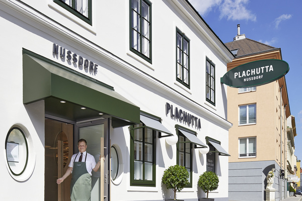 Ein Mann in einer Schürze steht an einem sonnigen Tag am Eingang des Restaurants Plachutta Nussdorf.