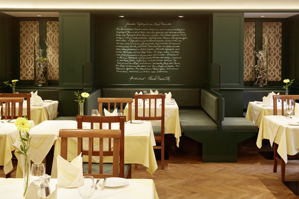 Elegant restaurant with wooden chairs, yellow tablecloths and handwritten lettering on a dark green wall.