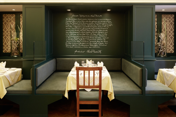 A restaurant stand with green walls, a wooden chair, a laid table and a handwritten text on the back wall.