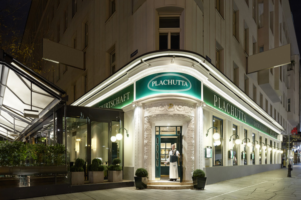 Elegant restaurant at night with green signs reading Plachutta and a person standing at the entrance.