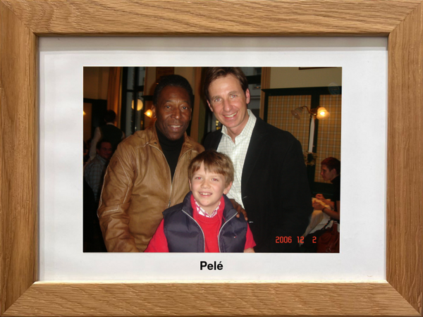 Drei Personen, darunter ein lächelndes Kind, posieren zusammen in einem Innenraum; gerahmtes Foto mit der Aufschrift Pelé.