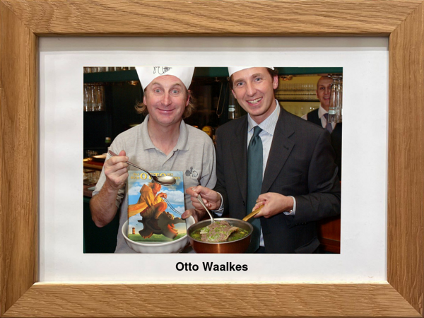 Two men in chefs hats, smiling and holding a cookbook and a pot of food, labeled with Otto Waalkes.