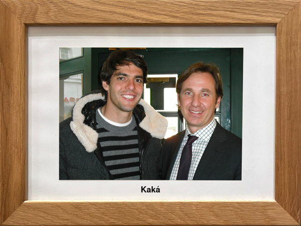 Zwei lächelnde Männer, einer im gestreiften Pullover und Mantel, der andere im Anzug, in einem hölzernen Bilderrahmen mit der Aufschrift Kaká.