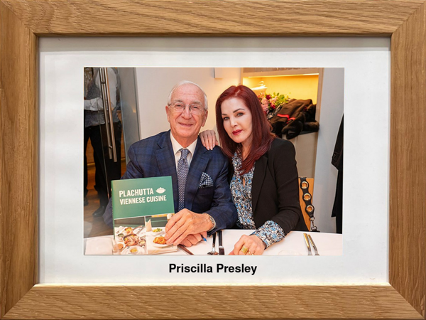 Ein älterer Mann und eine Frau sitzen an einem Tisch in einem Restaurant, an dem ein Schild mit der Aufschrift 'Plachutta Wiener Küche' hängt.