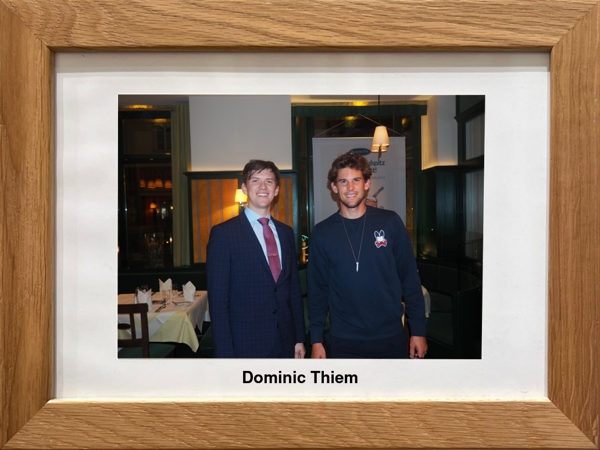 Zwei Männer stehen lächelnd in einem Haus, einer im Anzug und einer in Freizeitkleidung. Der Text darunter lautet: Dominic Thiem.