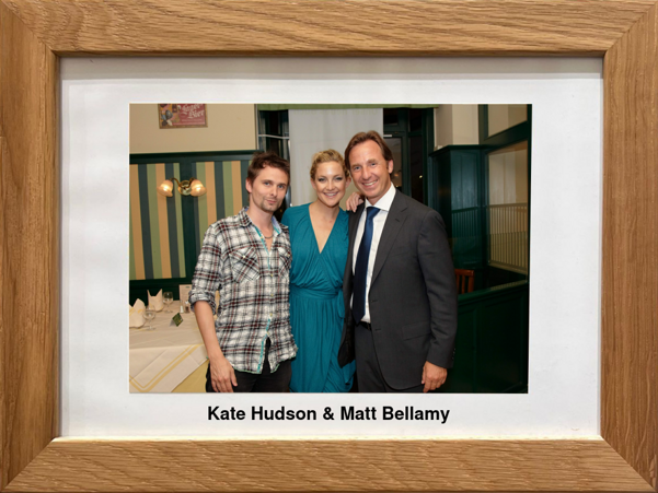 Drei Personen, die zusammen auf einem gerahmten Foto posieren, mit der Aufschrift Kate Hudson & Matt Bellamy unter dem Bild.