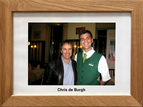 Zwei lächelnde Männer in einem Restaurant, einer trägt eine Lederjacke, in einem hölzernen Fotorahmen.