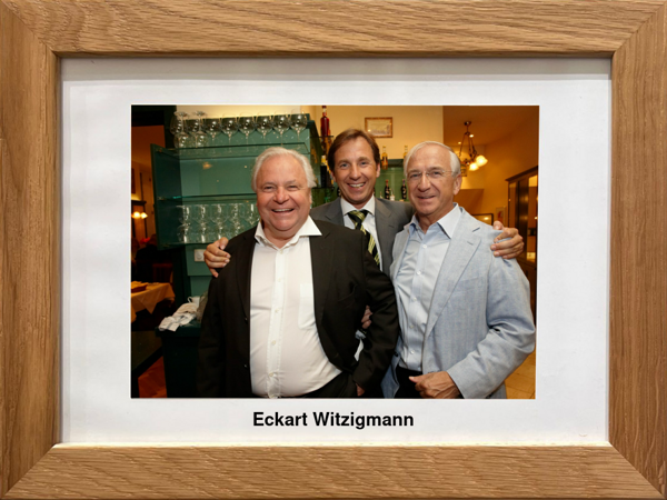 Three smiling men in suits pose together in a restaurant, framed with the name Eckart Witzigmann underneath.