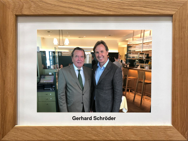 Two men in suits standing and smiling in a restaurant, framed photo with the inscription Gerhard Schröder.