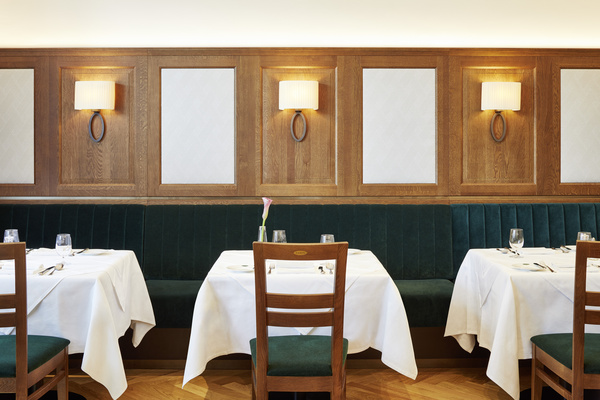 Vier weiß gedeckte Tische, grüne Stühle und eine Holzwand mit drei Leuchtern in einem modernen Restaurant.